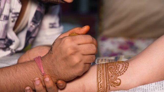 Artist applying intricate henna mehndi design on a woman's arm for a traditional wedding.