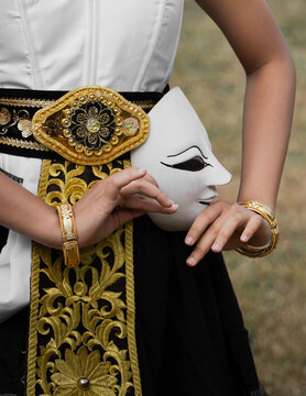 Close Up of Traditional Indonesian Female Dancer Holding White Mask with Golden Embroidery Outfit