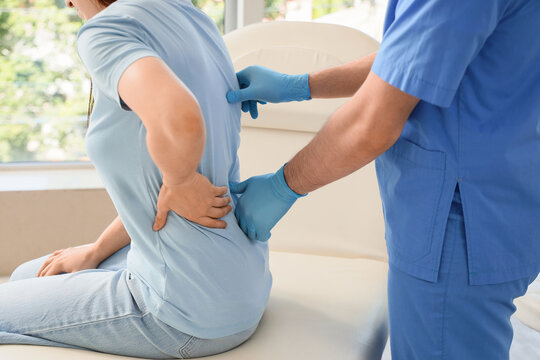 Patient with lower back pain receiving examination from a doctor in blue scrubs and gloves at a medical clinic, the medical professional is assessing the patients spine and back muscles