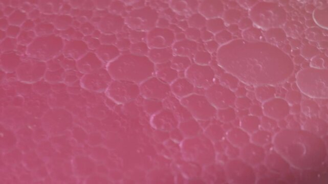Macro close up of pink acrylic paint cells moving across a liquid surface featuring abstract fluid texture organic patterns glossy finish and flowing motion