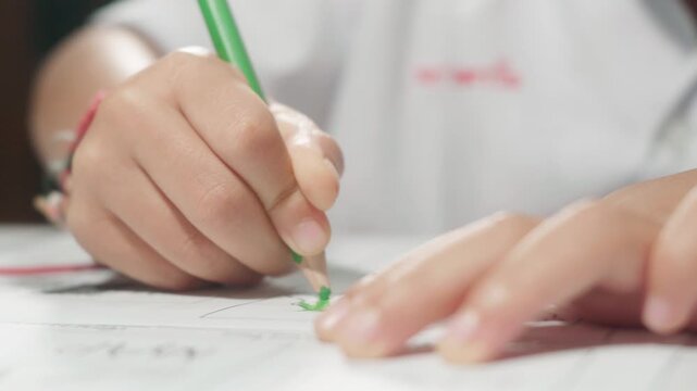 Close-up footage of a child's hand using a green colored pencil to color a worksheet, showing creativity, fine motor skills, concentration, early learning, and childhood education.