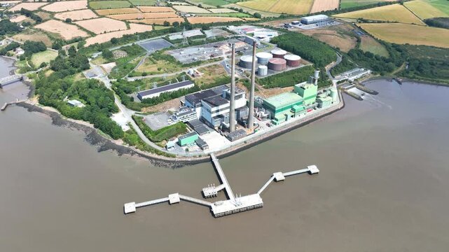 drone pullback capturing renewable energy power station on the River Suir, Wexford, Ireland. Detailed aerial views of electricity infrastructure with vibrant rural scenery.