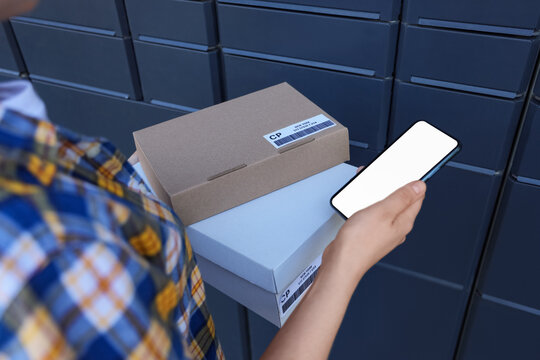Person holding packages and smartphone with blank screen near parcel locker for delivery service