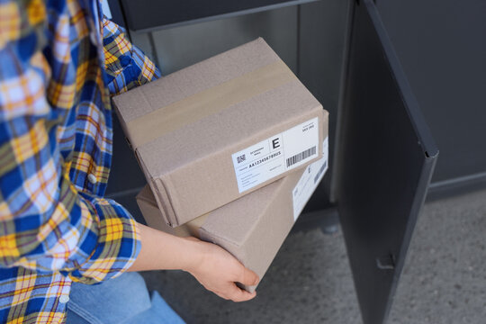 Person in plaid shirt retrieving two cardboard packages from a dark gray parcel locker, showing delivery and pickup service