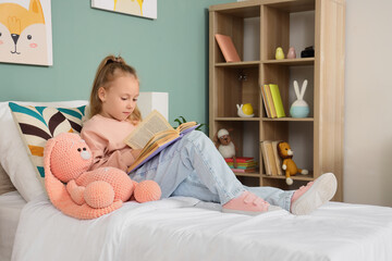 Young girl reading a book in bed with a plush toy, childhood education and leisure activity at home, the child is focused on the story © Pixel-Shot