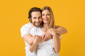 Fototapeta premium Happy Caucasian Couple Smiling And Embracing Each Other With Joyful Expressions, Showing Love And Affection, Standing Together In Studio Against Vibrant Yellow Background, Family Concept.