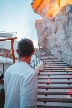 Cala en Porter, Spain - 12 May 2026: View of a man in a white shirt standing before the illuminated staircase leading to the Cova d'en Xoroi cliffside venue.