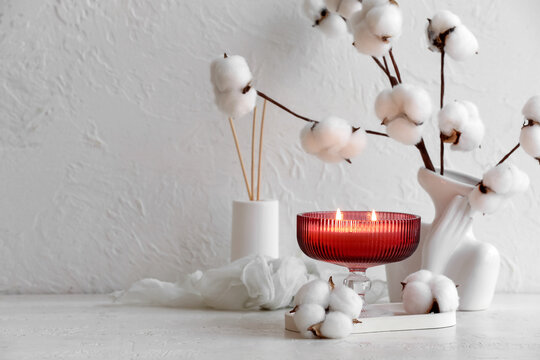 Red candle with cotton branches and aroma diffuser on a white textured background, cozy home decor concept, the arrangement creates a relaxing and warm ambiance
