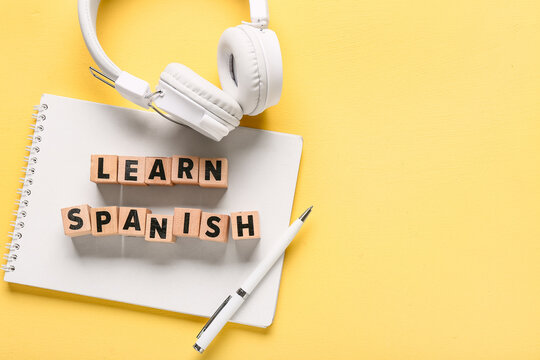 Learn Spanish wooden blocks with headphones and notebook on a yellow background, language education