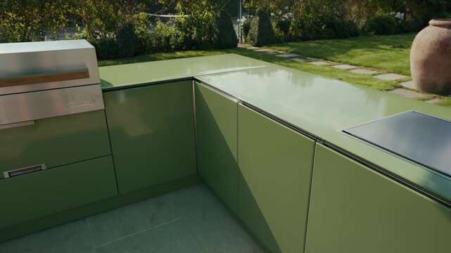 Modern green outdoor kitchen with stainless steel grill and reflective countertop