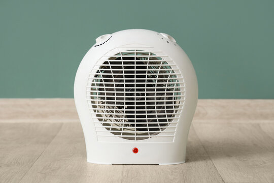 Electric fan heater on floor near turquoise wall in room