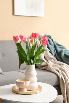 Vase with tulips and candle on table in living room decorated for Womens Day, closeup
