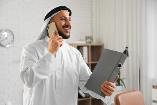Arab businessman with folder talking by mobile phone in office