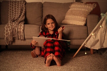 Fototapeta premium Cute little girl reading fairy-tale with teddy bear while sitting on floor at home