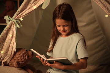 Fototapeta premium Cute little girl with book in play tent at home