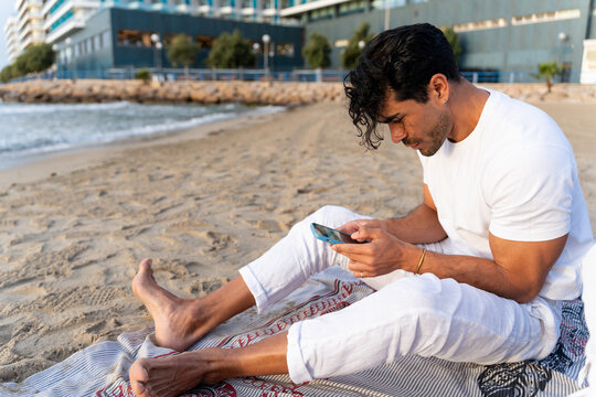 Man relaxing on beach, connecting with smartphone, enjoying leisure time