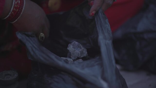Close up handheld shot of a woman's hands gently holding a rough chunk of natural rock salt against a blurred red traditional dress background