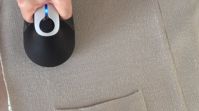 Top view hand removes pills from knitted clothing using fabric shaver. Textile pilling. Linting. Fabric lint, pilly, pellet, fluff. Fluff-ball remover