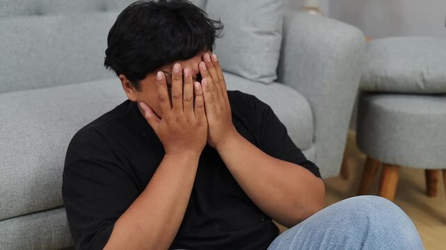 Depressed Asian overweight man covering his face at home