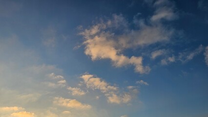 Fluffy white and golden-tinted cumulus clouds drift across a vivid blue sky during golden hour light. © Noa Badel