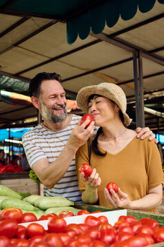 Couple Shopping at Farmers Market Smiling While Choosing Fresh Tomatoes With Asian Woman And Man