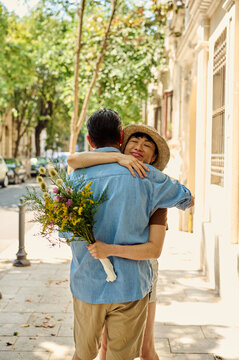 Couple Hugging On Sunny City Street With Bouquet &mdash; Asian Woman Embracing Partner In Denim