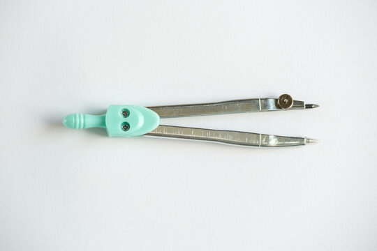 Mint green school compass for drawing and geometry on a light neutral background, top view.