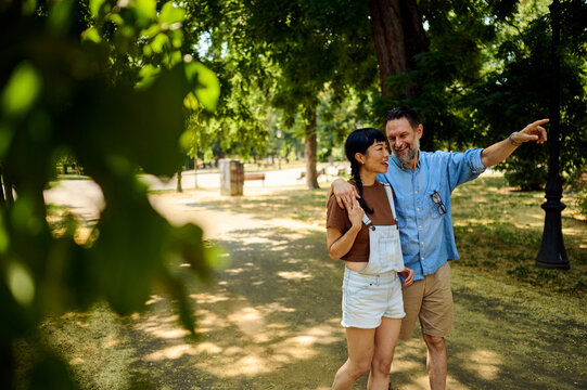 Couple Walking in Sunny Park Pointing and Laughing During a Casual Summer Stroll Together