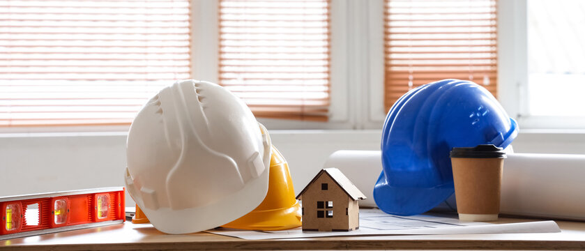 Construction site safety helmets blueprints and a small house model on a wooden desk architecture and real estate development