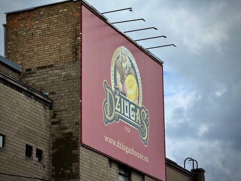 Billboard on a brick building in Lithuania features an advertisement for Džiugas cheese. The ad showcases the brand name in ornate lettering with an illustration of a bearded man 