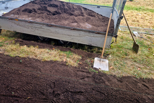 a trailer full of dark soil or compost and a garden shovel stuck in the grass next to it. You can specify what you plan to do with this soil: lawn establishment, raised beds, landscaping