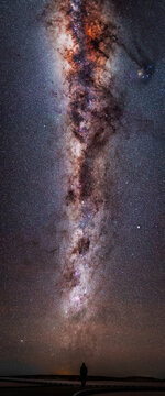 Panoramic view of a lone figure standing beneath the immense sweep of the Milky Way with its glowing star fields and dark dust lanes strecthing across the night sky, Lake Tyrrell, Victoria, Australia
