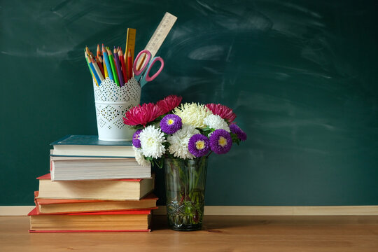 school stationery, flowers bouquet and stack of books on table against chalkboard. symbol of beginning of the school year, teacher's day, Knowledge Day. education, back to school,1 September concept