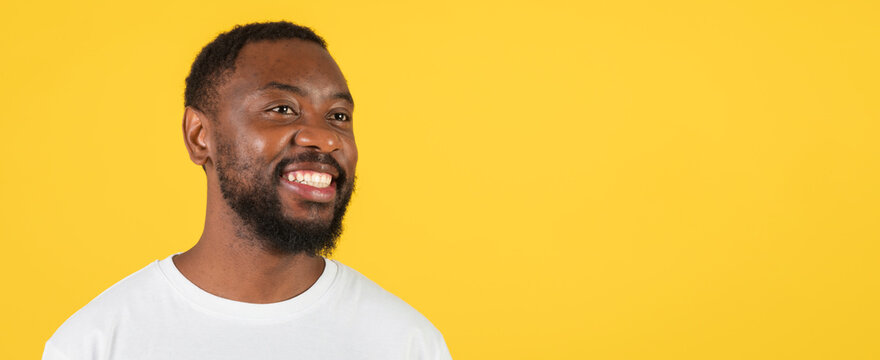 Smiling Black Male Adult In His 30s Looking To Side With Joyful Expression Against Vibrant Yellow Background, Carrying Positive Energy In Professional Setting. Business Concept.