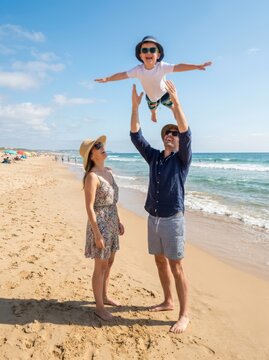 Family playing together throwing son in air on beach