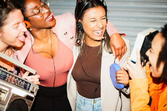 Group of multiracial girls having fun together listening music while taking photo with a vintage instant camera - Party, nightlife and peoople lifestyle concept - Main focus on center woman face