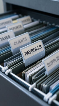 Filing cabinet with hanging folders labeled "Payrolls," "Clients," "Taxes," showcasing organization and financial record-keeping, ideal for business concepts.