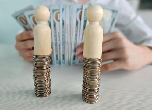 Money and coins are stacked next to wooden figures showing a financial concept