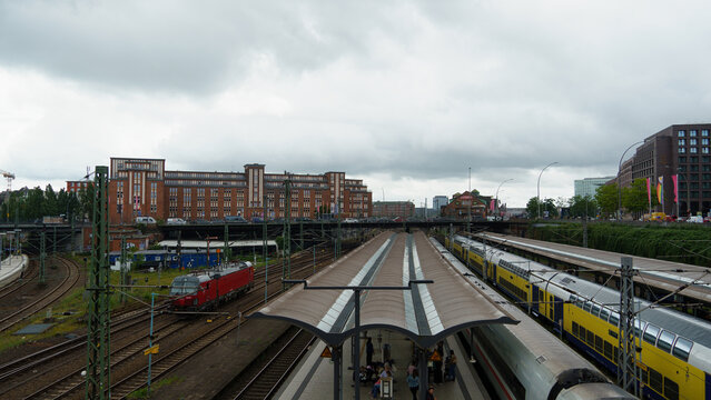 Hamburg, Germany - 22 July 2026: View of Hamburg Hauptbahnhof train station with a red locomotive and yellow passenger trains on tracks under a cloudy sky.