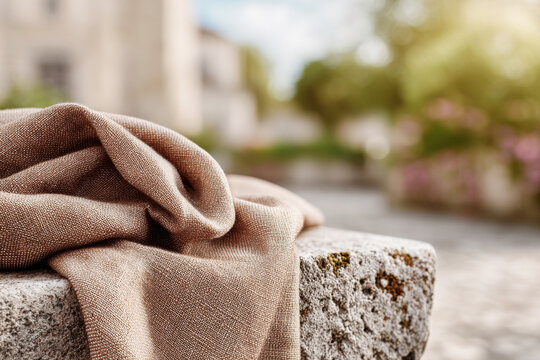 Draped brown linen fabric over rough stone block outdoors with blurred urban background in sunlight