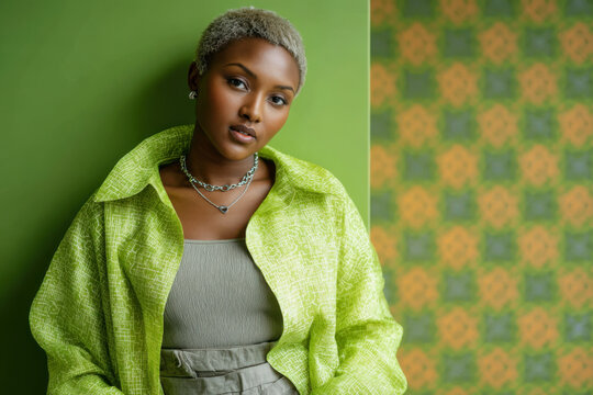 African American woman with short bleached hair wearing lime green patterned shirt and chain necklace against green wall