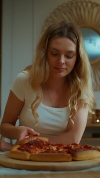 Woman standing by the kitchen island and grabbing a slice of the fresh hot homemade pepperoni pizza she prepared at home