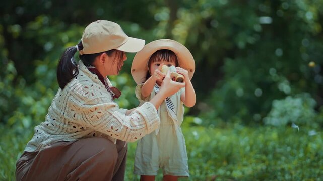 Asian mother teaching toddler daughter to use binoculars while observing butterflies in Kaeng Krachan, Thailand, family nature exploration and outdoor learning