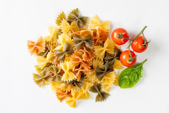 A vibrant assortment of colorful farfalle pasta served with fresh cherry tomatoes and a basil leaf on a clean white background.
