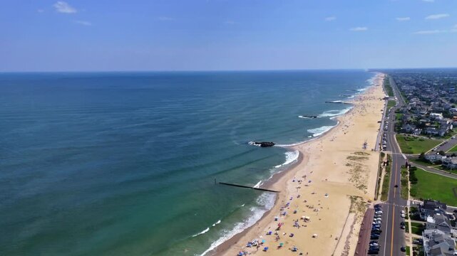 Aerial wide shot captures people on Belmar Beach with ocean waves under a clear sky