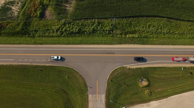 Aerial topdown shot of a two lane rural highway in Shiocton, Wisconsin, featuring semi-truck with a trailer and passenger cars driving past green farm fields.