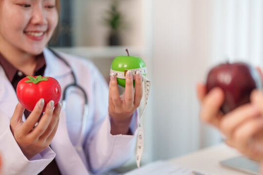 Nutrition consultant holding green apple with tape measure and tomato in clinic