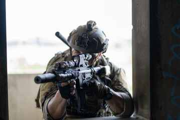 Fototapeta premium Special force soldier aim rifle through window frame during tactical operation. Army operative in helmet prepare to shoot target in building