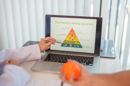 Nutrition consultant explaining healthy eating pyramid on laptop screen during medical consultation