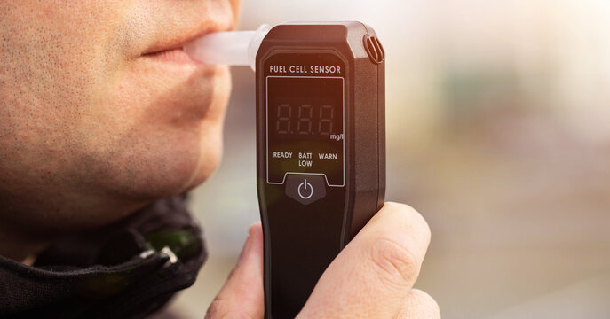 Man Blowing Into Breathalyzer Mouthpiece Outdoors. Closeup Of Male Driver Performing Alcohol Test.